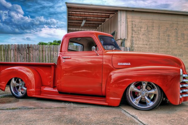 A red pickup truck is parked near a wooden building