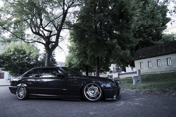 Black understated BMW E36 on the background of the house