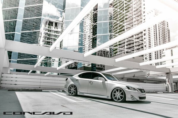 A silver sparkling car in an open parking lot with a view of the skyscrapers