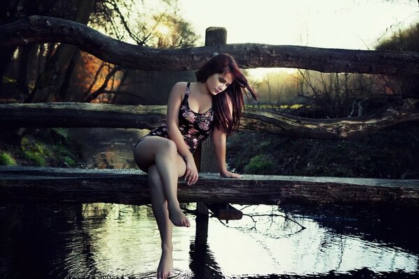 Brunette assise sur un pont au coucher du soleil