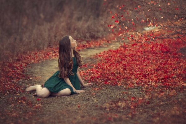 Una ragazza in un vestito verde si siede nel fogliame