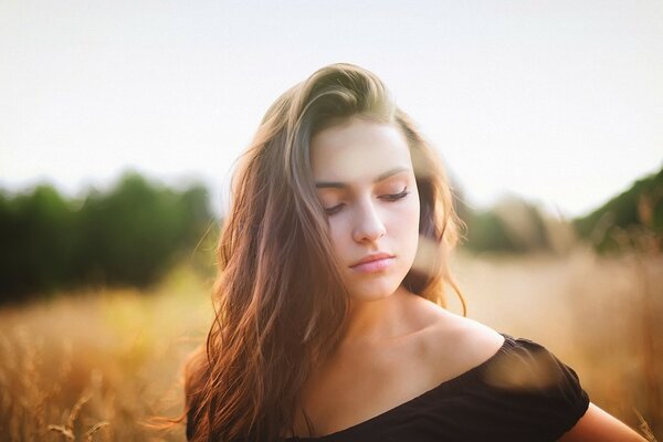 A calm girl stands in a field and looks down