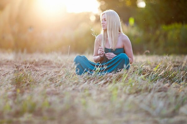 A girl in the field is sitting on the grass