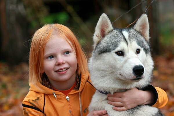 A little red-haired girl hugs a dog