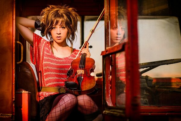 Piękna dziewczyna siedzi przy oknie ze skrzypcami w rękach