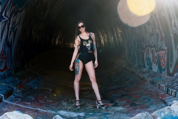 A girl with a tattoo on her leg is standing in a tunnel