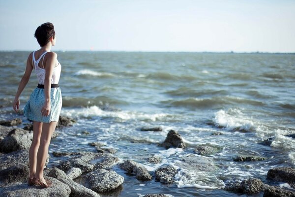 The girl is standing with her back on the rocks by the seashore