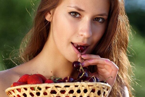 Mädchen mit einem Korb mit Erdbeeren und Kirschen im Mund