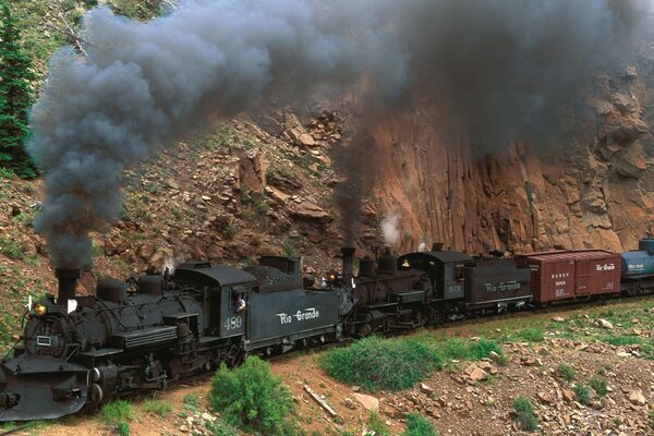 Tren de carga negro cabalga sobre rieles en las montañas
