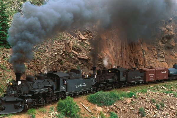 Treno merci nero cavalca su rotaie in montagna