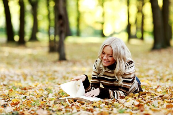 Rubia leyendo en las hojas de otoño