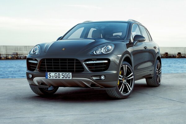 A black Porsche stands against the background of a dam