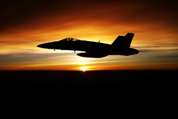 At sunset, the silhouette of a fighter jet flies