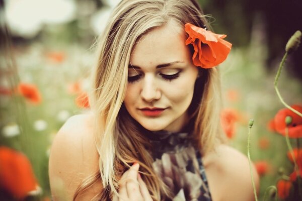 Blonde Mädchen im Mohnfeld posiert mit einer Blume, die im Haar erstochen wird