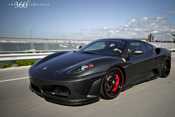 A black ferrari with red wheels rides on a bridge