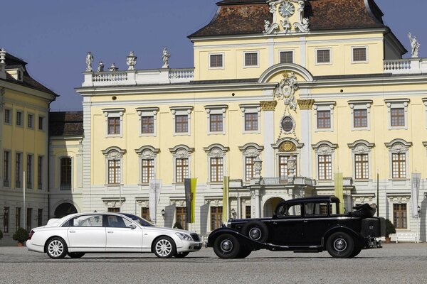 Un Maybach blanco y un coche negro en el fondo de un edificio