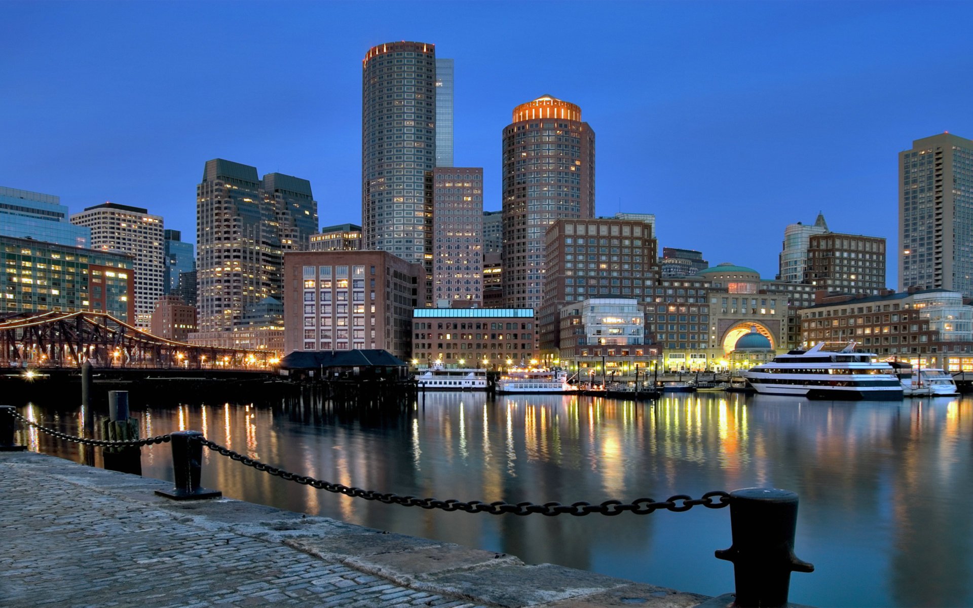 the city the evening lights chain fence the ship boat river blue sky building home the light in the windows skyscrapers megapolis bridge promenade the sidewalk water surface reflection the lights of the city