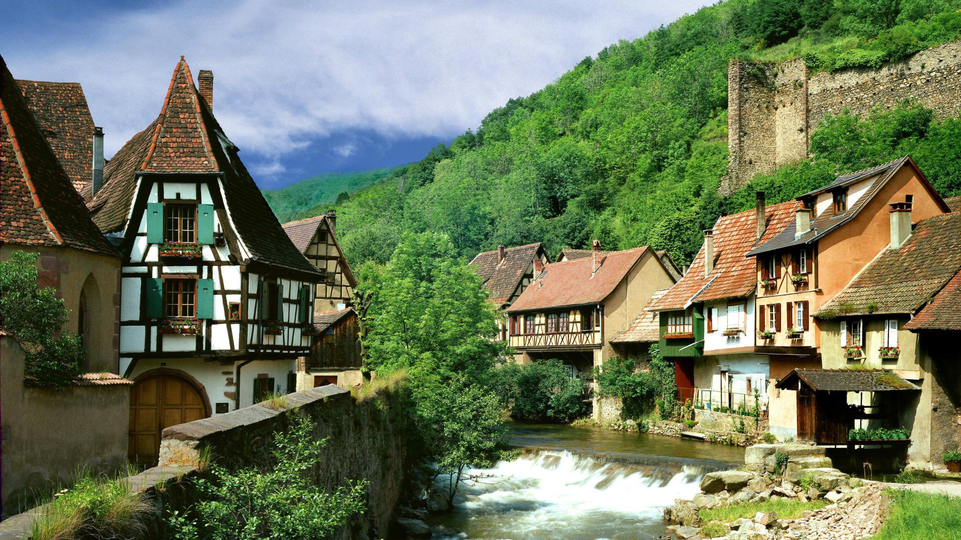 häuser am wasser sommer landschaft berge grün vegetation dickicht häuser fluss strom siedlung himmel wolken dächer