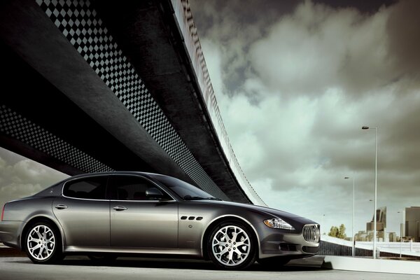 Silver Maserati car under the bridge, gray sky