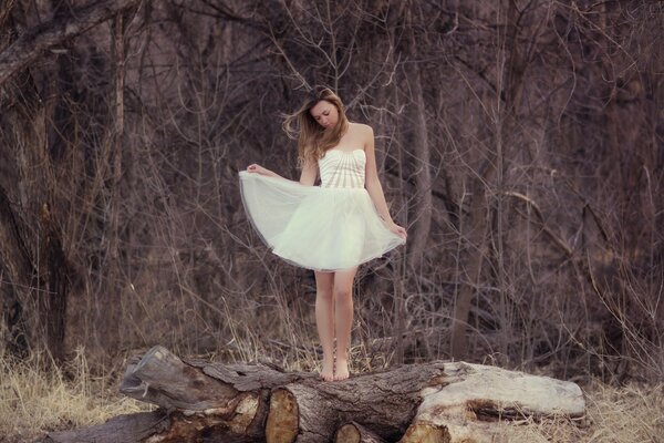 A girl in a white dress by a log