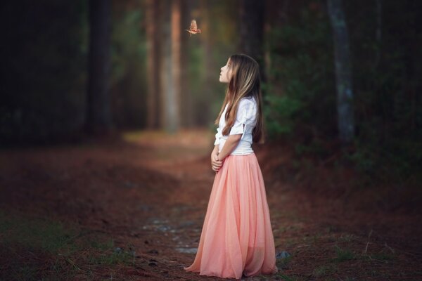 A girl in a pink skirt in the forest with a bird