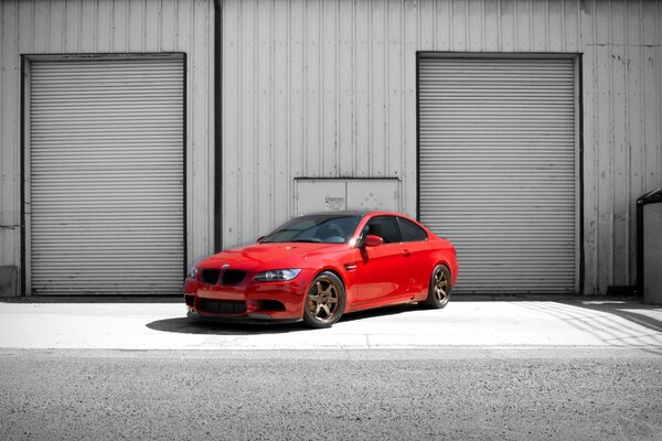 Red tinted BMW car on the background of a building with two gates and a panel