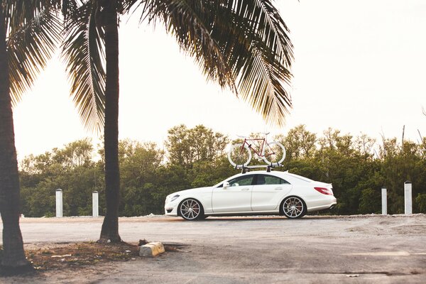 A white Mercedes with a trunk on which a bicycle is fixed