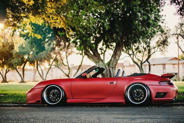 Auto rossa convertibile Porsche e alberi verdi