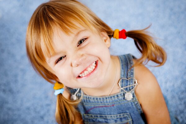 A joyful girl with ponytails in a denim overalls