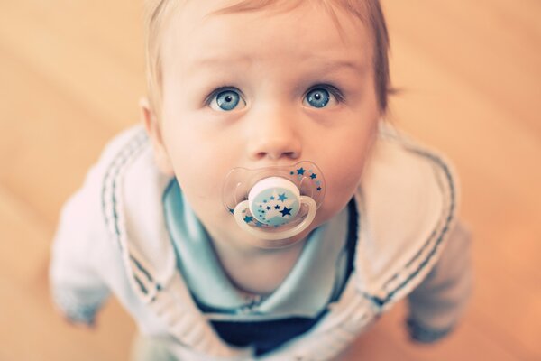 A child with blue, beautiful eyes sucks a pacifier