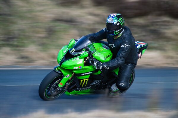 Un motocycliste portant un casque sur une Kawasaki verte entre dans le virage