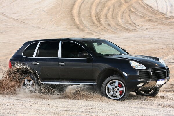 Porsche Cayenne negro cabalga sobre la arena en el desierto