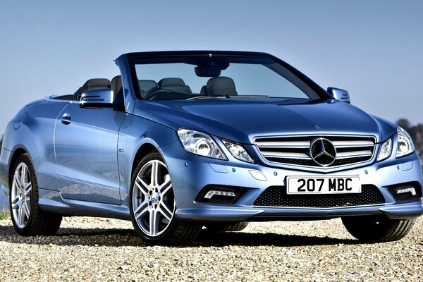 Hermoso coche azul marca Mercedes clase convertible junto al río en el fondo del cielo azul