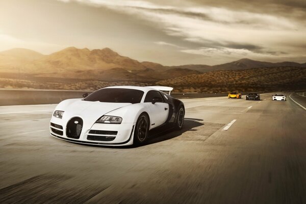 Black-and-white tinted car in the rays of the sun against the background of mountains and white, black and orange cars