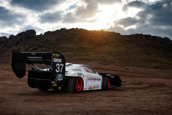 A sports car rides on the sand at sunset