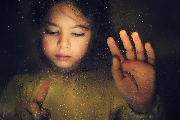 The girl watches the drops run down the glass