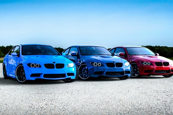 Red, blue and blue BMW parked in a vacant lot