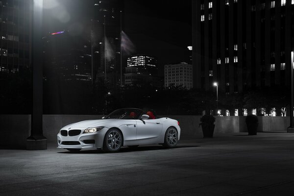 White BMW with headlights on under a plywood pole