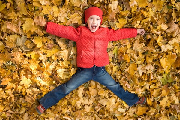 Un enfant en veste rouge se baigne dans les feuilles