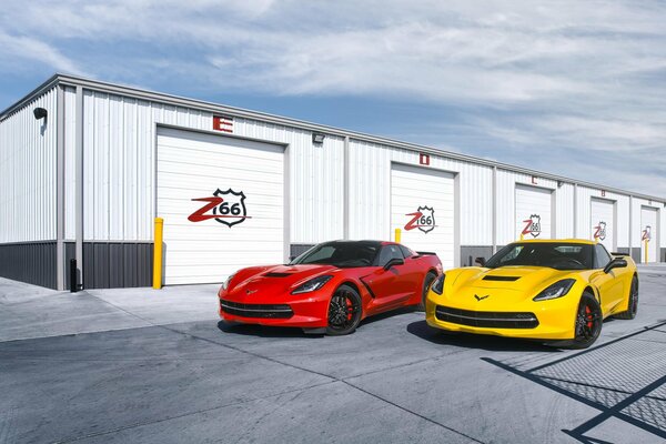Auto sportive luminose sullo sfondo di garage sotto il cielo blu. Chevrolet Corvette rossa e gialla vicino ai garage