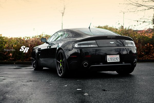 A black Aston Martin car. Wet asphalt with a sunset sky