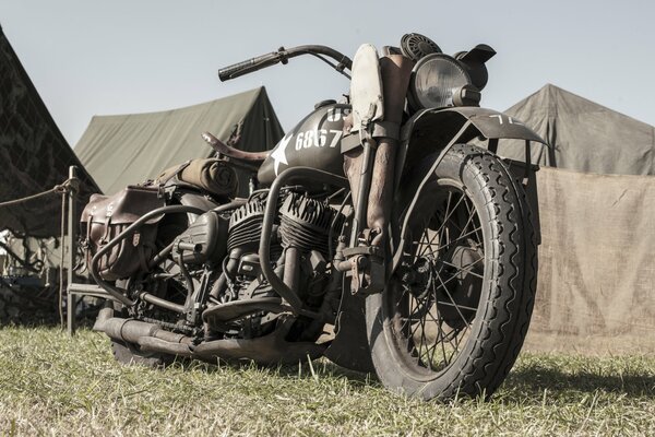 A motorcycle from the Second World War stands among the tents and waits for its rider