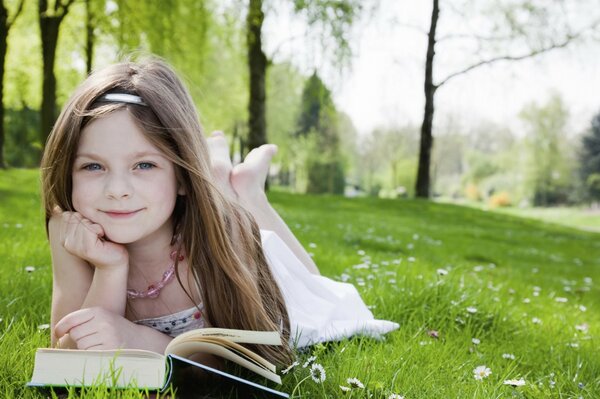 A girl with a book is lying on the lawn