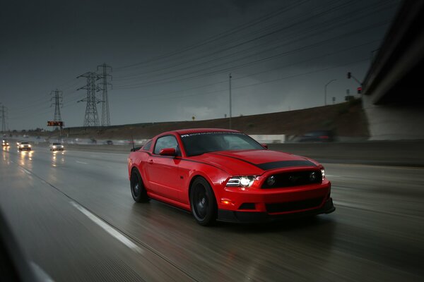 Voiture rouge Ford Mustang sur la route sur fond de ciel orageux