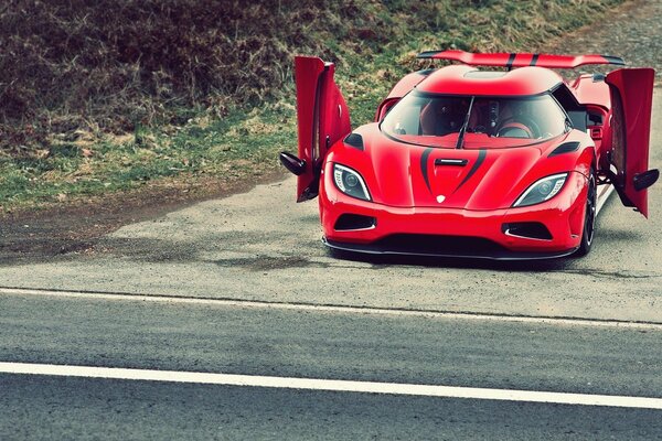 Red car with raised doors on the side of the road