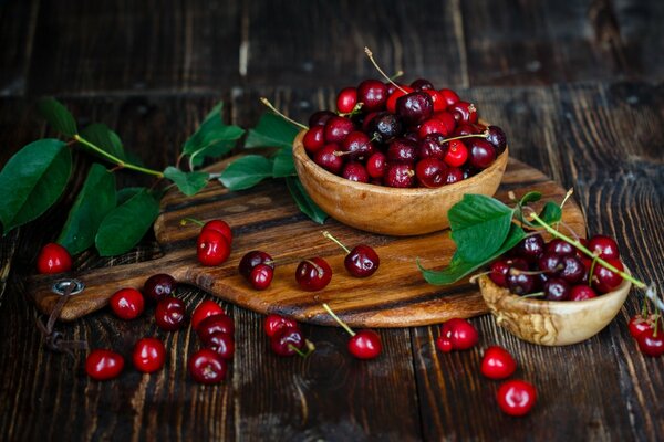 Sur une planche de bois, il y a deux assiettes en bois avec des cerises