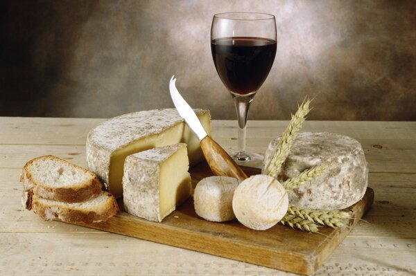 A glass of wine, pieces of cheese and bread