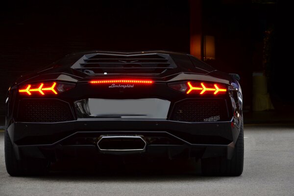 The back of a black lamborghini with the headlights on