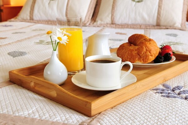 A glass of orange juice, a cup of tea and a booth on a tray on the bed