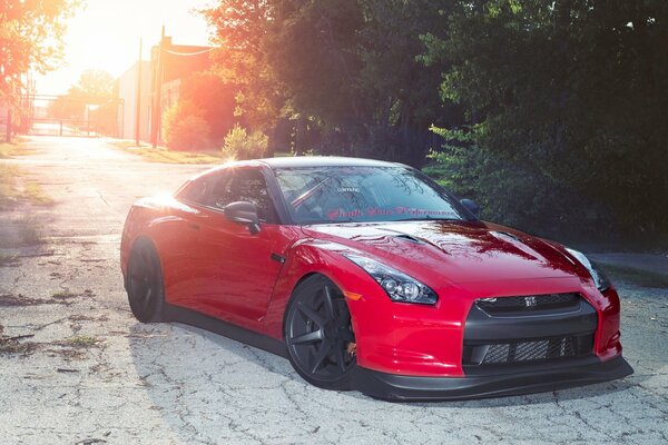 Coche deportivo coupé rojo en el fondo de la puesta de sol y los árboles